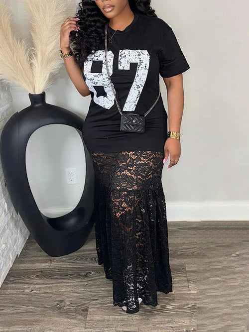 Woman wearing a black t-shirt with white numbers and a black lace skirt, standing next to a black vase.